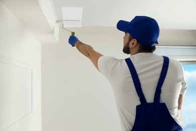 Handyman painting ceiling with white dye indoors, back view