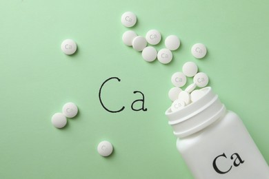 Flat lay composition with calcium supplement pills on light green background