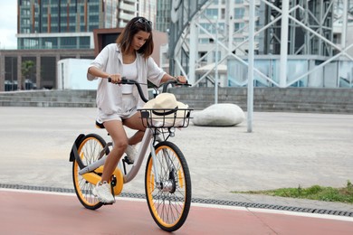 Beautiful young woman riding bicycle on lane in city. Space for text