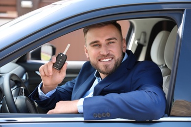 Businessman with car key sitting in new auto outdoors