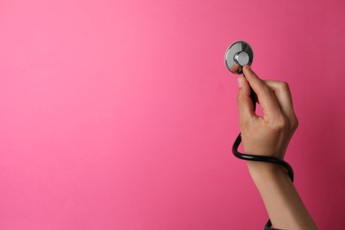 Woman holding stethoscope on pink background, closeup. Space for text
