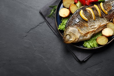 Tasty homemade roasted crucian carp with garnish on black table, top view and space for text. River fish