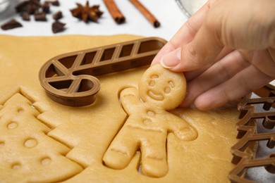 Photo of Christmas treat. Woman holding unbaked man shaped cookie at light table, closeup
