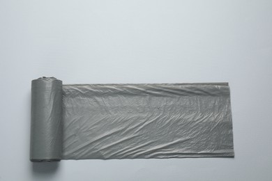 Photo of Roll of grey garbage bags on light background, top view