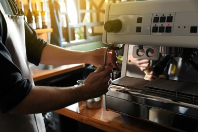 Photo of Barista cleaning coffee machine steam wand with rag on bar counter, closeup