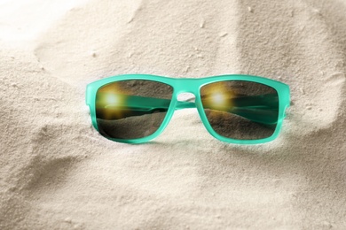 Stylish sunglasses on white sand. Fashionable accessory
