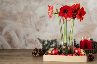 Photo of Beautiful red amaryllis flowers and Christmas decor on wooden table. Space for text