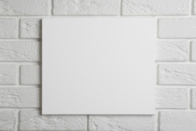 Blank canvas hanging on white brick wall, space for text