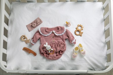 Flat lay composition with cute baby clothes and accessories on white bedsheet in crib