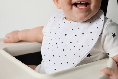 Cute little baby wearing bib in highchair on white background, closeup