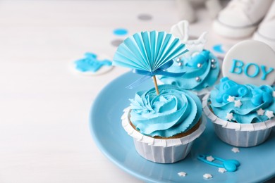 Delicious cupcakes with light blue cream and toppers for baby shower on white wooden table