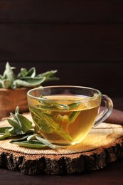 Cup of aromatic sage tea and fresh leaves on wooden table. Space for text
