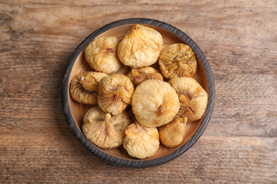 Tasty dried figs in plate on wooden table, top view
