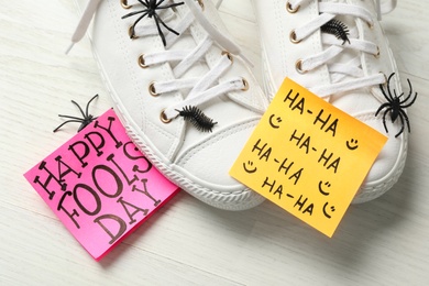 Shoes with fake spiders, bugs and Happy Fools' Day note on white wooden table, closeup