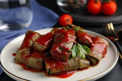 Delicious stuffed grape leaves with tomato sauce on table, closeup