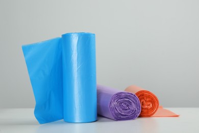 Photo of Rolls of different color garbage bags on table against light background