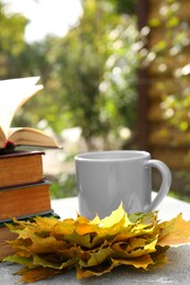 Yellow maple leaves, books and cup of tea on light gray table. Autumn atmosphere