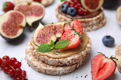 Tasty crispbreads with peanut butter, figs and berries on light table, closeup