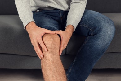 Man suffering from leg pain on sofa indoors, closeup