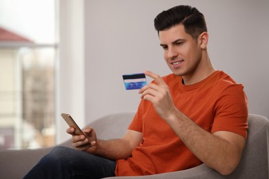 Photo of Man using smartphone and credit card for online payment on sofa at home