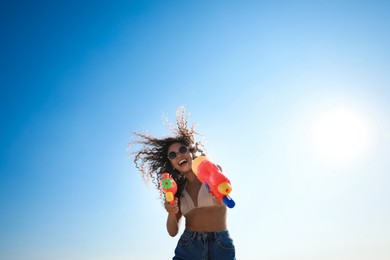 African American woman with water guns against blue sky, low angle view