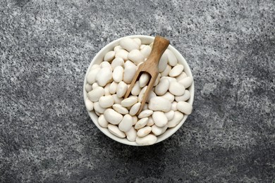 Raw white beans and scoop in bowl on grey table, top view