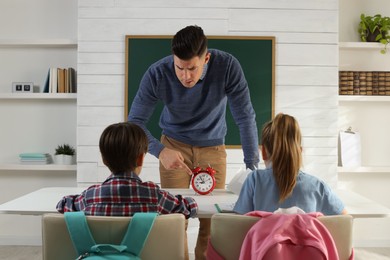 Teacher with alarm clock scolding pupils for being late in classroom
