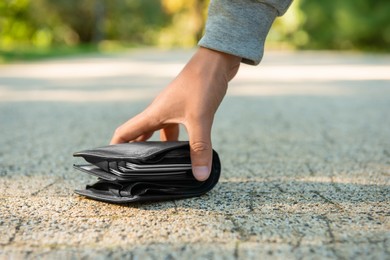 Man picking lost wallet from ground outdoors, closeup. Space for text