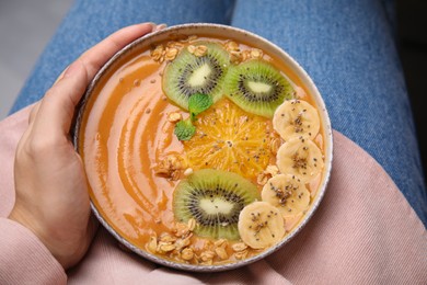 Woman holding bowl of delicious fruit smoothie with fresh banana, kiwi slices and granola, top view