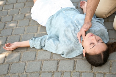 Young man checking pulse of unconscious woman outdoors. First aid