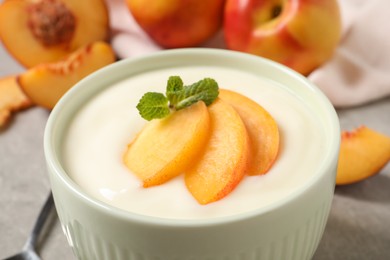 Delicious yogurt with fresh peach and mint in bowl on table, closeup