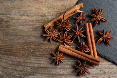 Aromatic cinnamon sticks and anise stars on wooden table, flat lay. Space for text