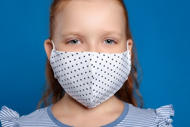 Photo of Preteen girl in protective face mask on blue background, closeup