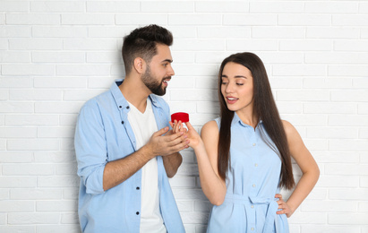 Young woman with engagement ring making marriage proposal to her boyfriend near white brick wall
