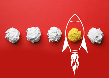 Business startup concept. Colorful crumpled papers and drawn rocket on red background, flat lay