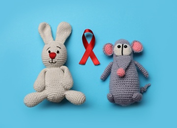Cute knitted toys and red ribbon on blue background, flat lay. AIDS disease awareness