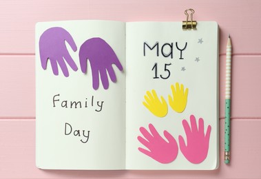 Notebook with text Family Day May 15 and paper cutouts on pink wooden table, flat lay