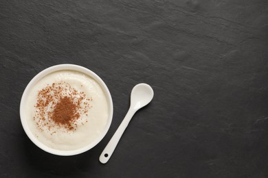 Delicious semolina pudding with cinnamon and spoon on black table, flat lay. Space for text