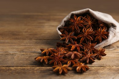 Overturned bag with aromatic anise stars on wooden table, closeup. Space for text