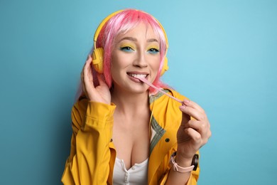 Fashionable young woman in pink wig with headphones chewing bubblegum on yellow background