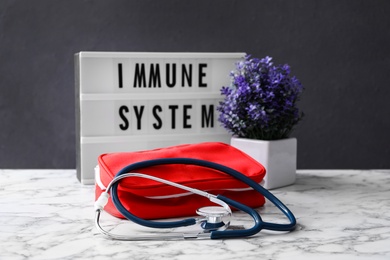 Lightbox with words Immune System, flowers and first aid kit on white marble table