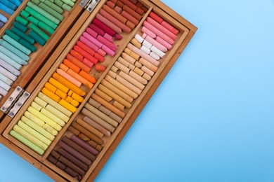 Set of soft pastels in wooden box on light blue background, top view with space for text. Drawing material