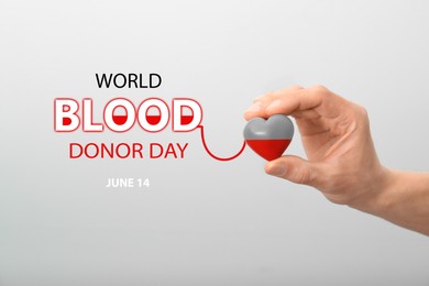 Image of World Blood Donor Day. Man holding small red heart on light background, closeup