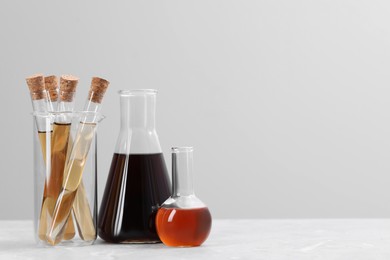 Photo of Different laboratory glassware with brown liquids on white table against light background. Space for text