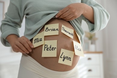 Pregnant woman with different baby names on belly indoors, closeup