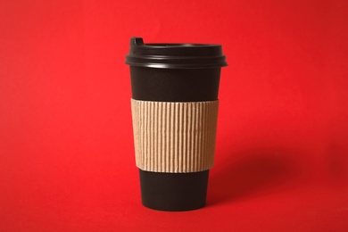 Takeaway paper coffee cup with cardboard sleeve on red background, closeup