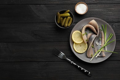 Photo of Salted herring fillets served with green onions and lemon on dark wooden table, flat lay. Space for text
