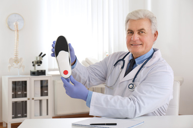 Senior male orthopedist showing insole in clinic