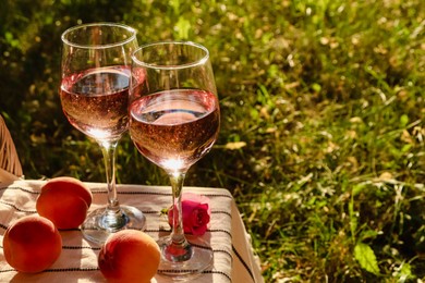 Photo of Glasses of delicious rose wine, flower and peaches on white picnic blanket outside. Space for text