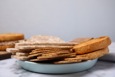 Rye crispbreads, rice cakes and rusks on white marble table, space for text